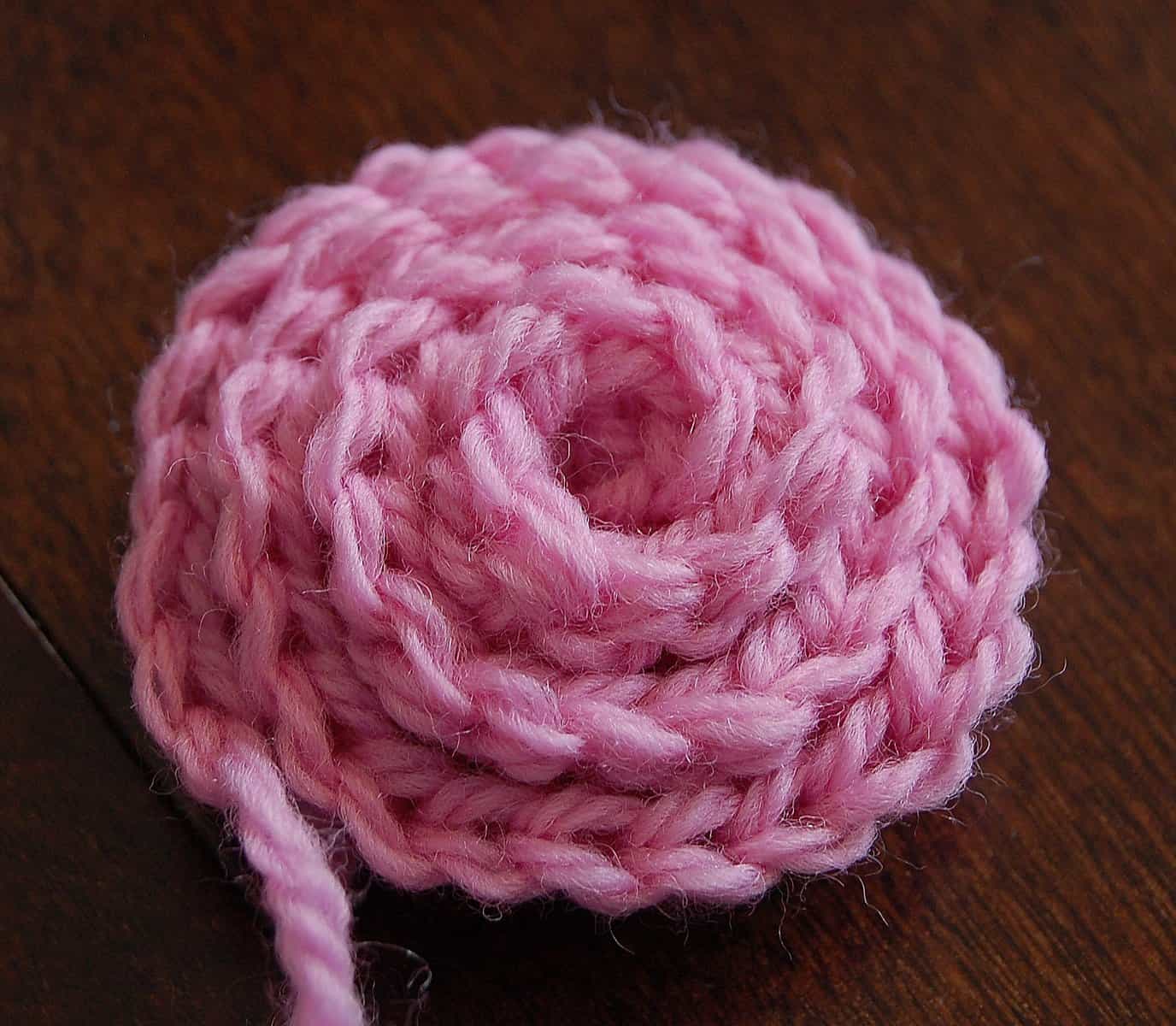 Medium pink crochet rose with tail of yarn not yet woven in.