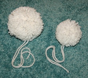 Two white yarn poms laying on green carpet.