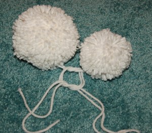 One small and one big white yarn pom laying on carpet.