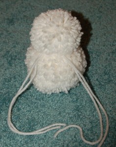 Two white yarn poms tied together to form a snowman.