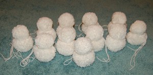 Nine small white yarn pom snowmen standing on carpeted floor.