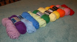 Skeins of yarn in the colors of the rainbow laying on carpeted floor.