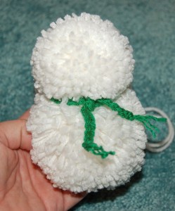 Small yarn pom snowman with green scarf tied around its neck.