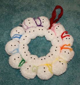 Snowman yarn pom wreath laying on carpeted floor.