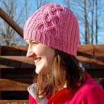 Girl modeling pink ribbed crochet hat with heart cables on side.