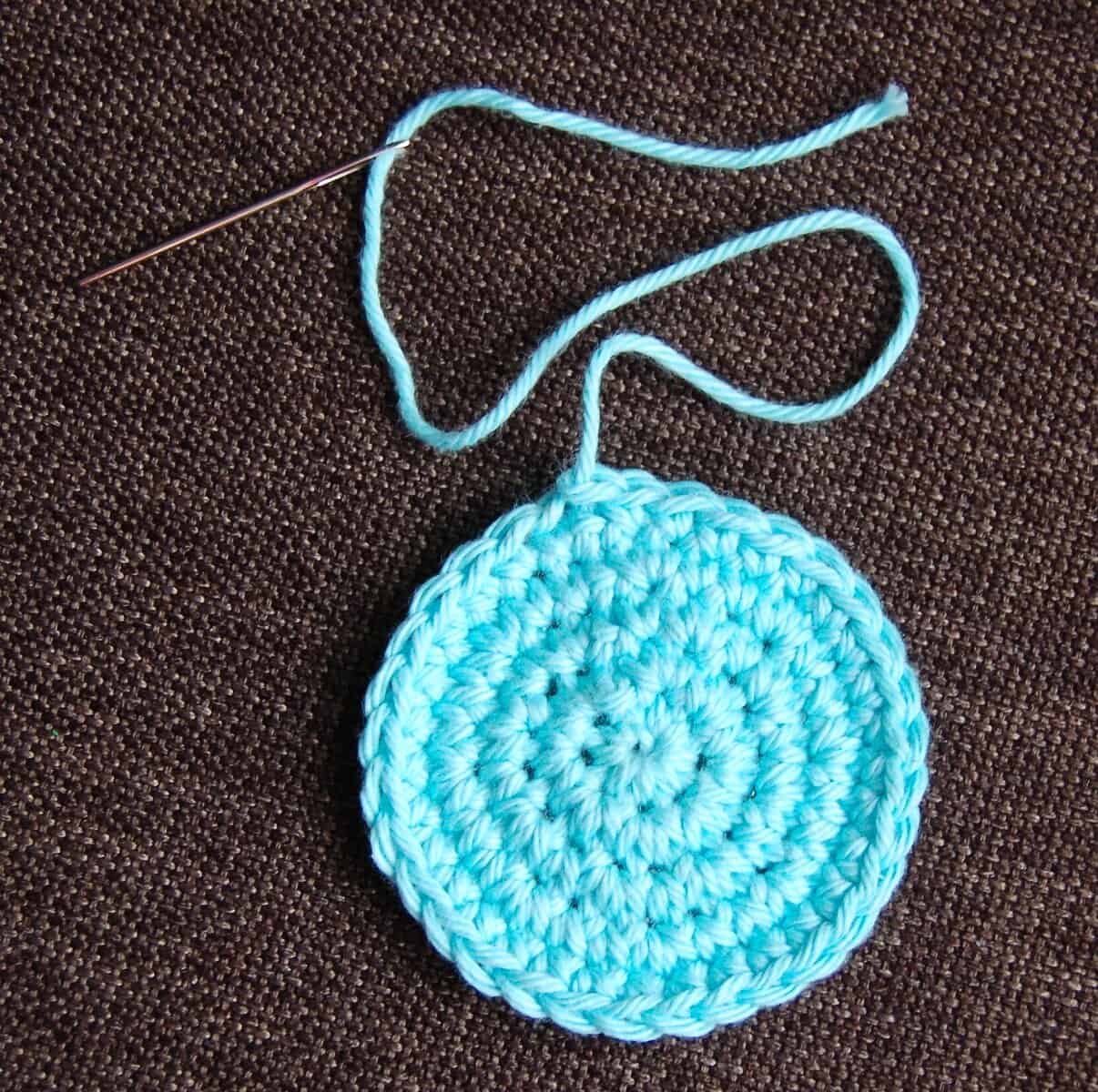 Small blue crochet circle and yarn needle laying on brown surface.