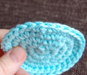 Hand holding small blue crochet circle to show crochet invisible join.