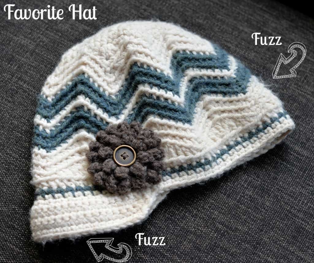 Chevron crochet newsboy hat with brown flower laying on brown couch.