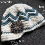 Chevron crochet newsboy hat with brown flower laying on brown couch.