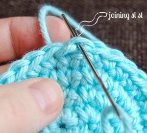 Yarn needle weaving blue yarn into one loop to create invisible join seam.