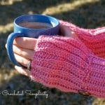 Pink ribbed fingerless crochet mitts and hands holding hot coffee.