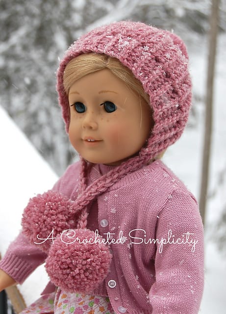 American girl doll modeling pink winter crochet hat with yarn poms.