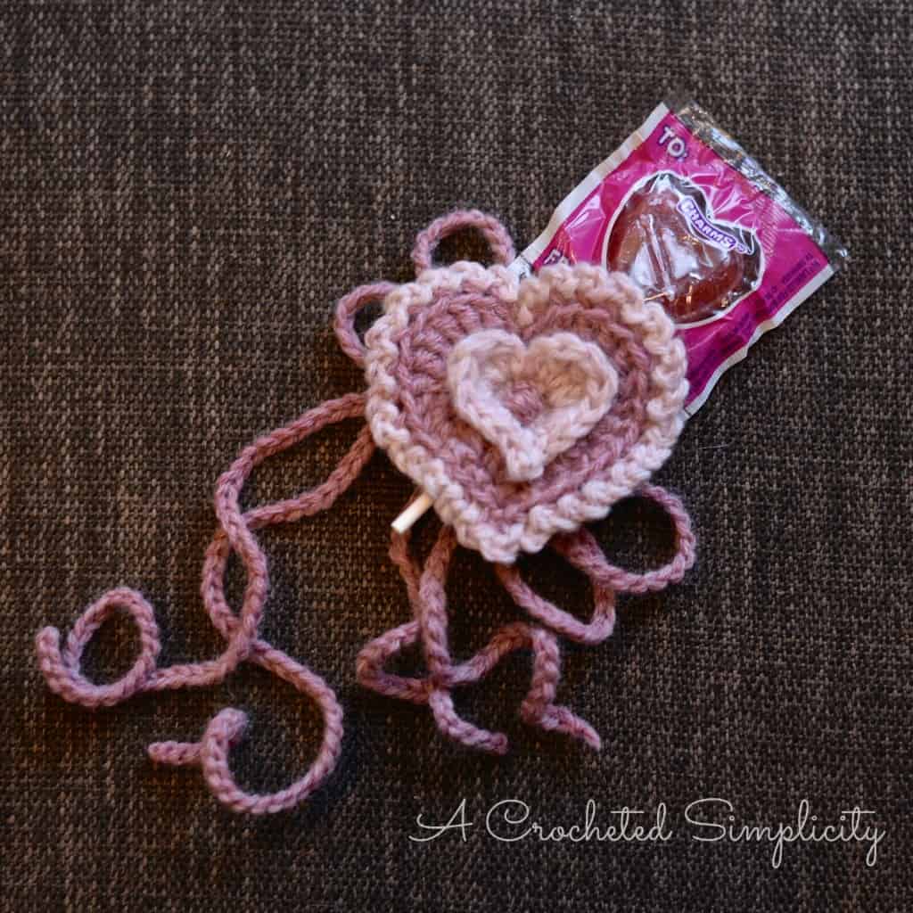 Crochet treat holder with two pink hearts holding a heart shaped sucker.