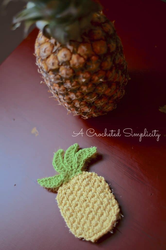 Pineapple crochet dish scrubby sitting on red table with pineapple fruit.