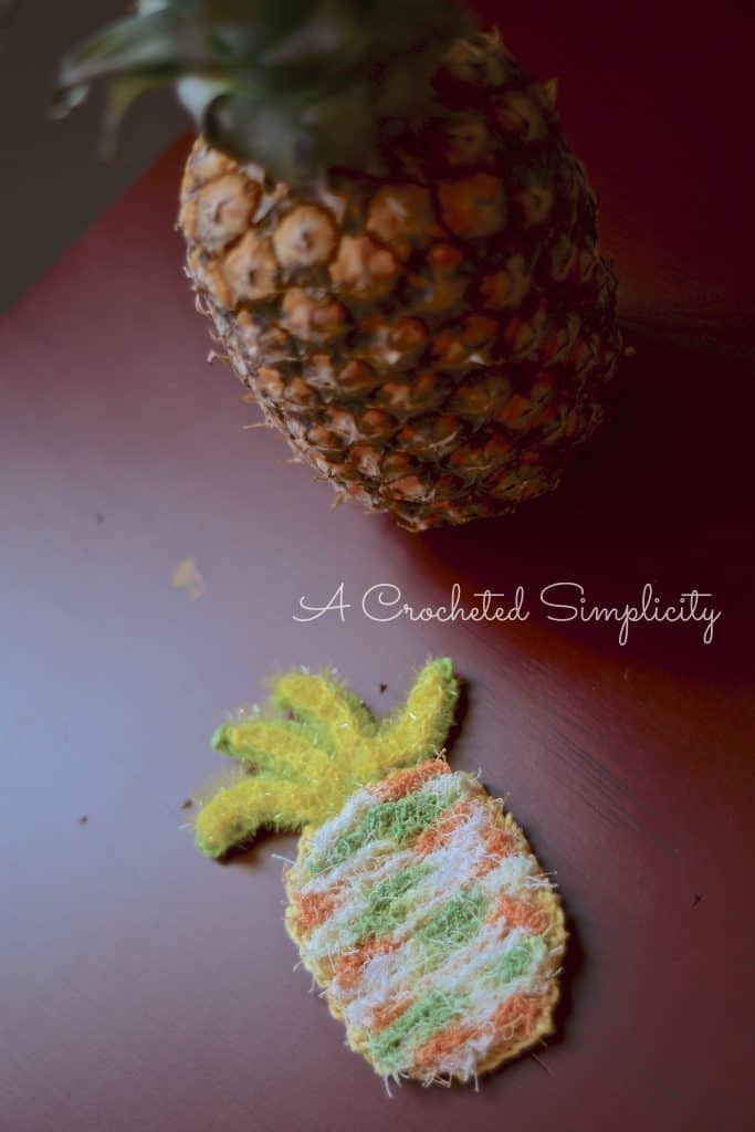 Pineapple scrubby and pineapple fruit on dark red table.