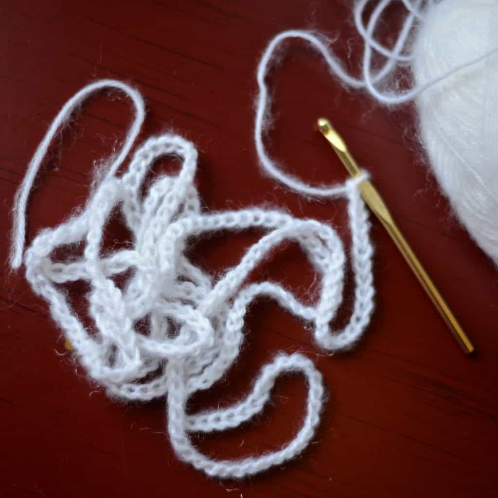 Lone white crochet chain with gold crochet hook.