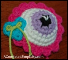 Crochet eyeball with pink edging and blue heart.