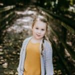 Young girl wearing a light grey crochet cardigan with pockets.