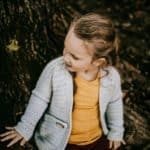 Young girl wearing a light grey crochet cardigan with pockets sitting on a tree.