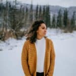 Woman modeling a gold crochet cardigan with pockets in the mountains