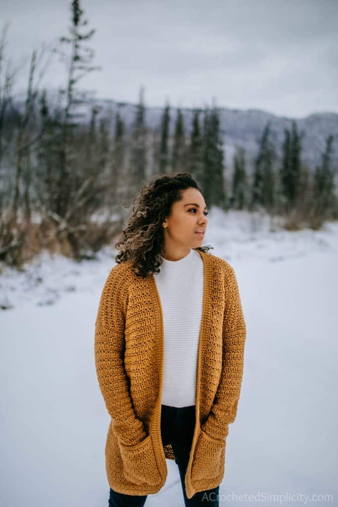 Woman modeling a gold crochet cardigan with pockets in the mountains