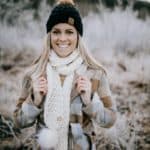 Young woman wearing a cream color chunky crochet scarf with faux fur poms on each end.