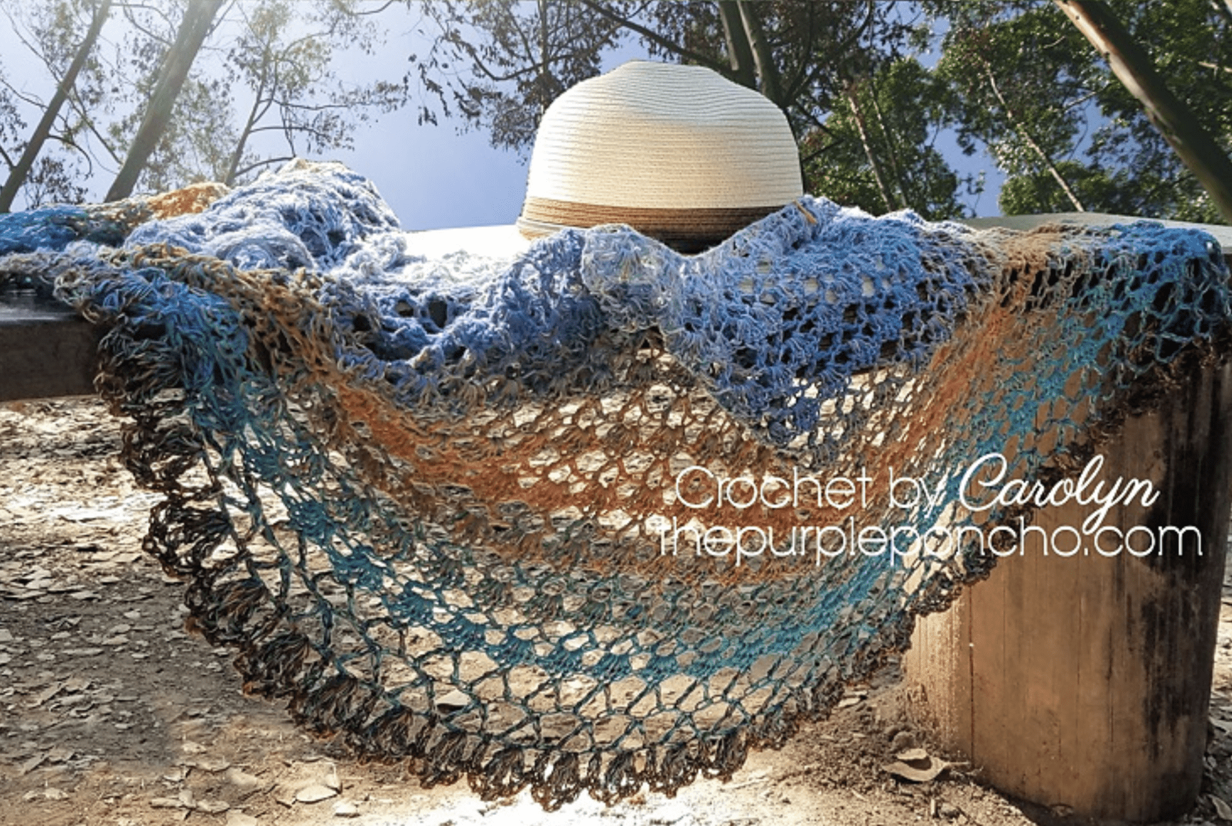 Lacey crochet shawl draped over driftwood bench with a sun hat laying on top.