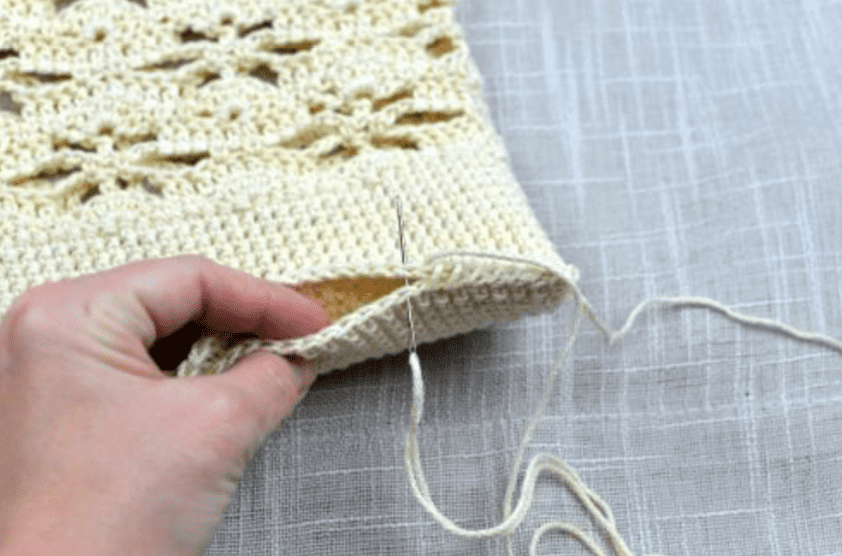 Close up showing bottom of crochet tote bag being seamed with a whipstitch.