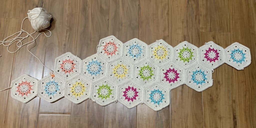Colorful crochet hexagons seamed together on a wooden floor.