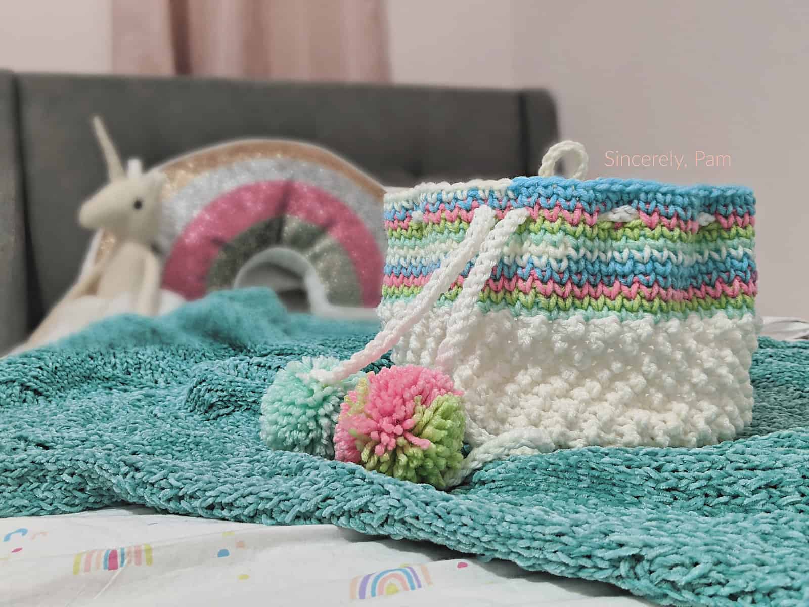 Small white crochet basket with drawstring tie and yarn poms.