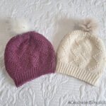 Two crocheted slouch hats laying on white bedspread.