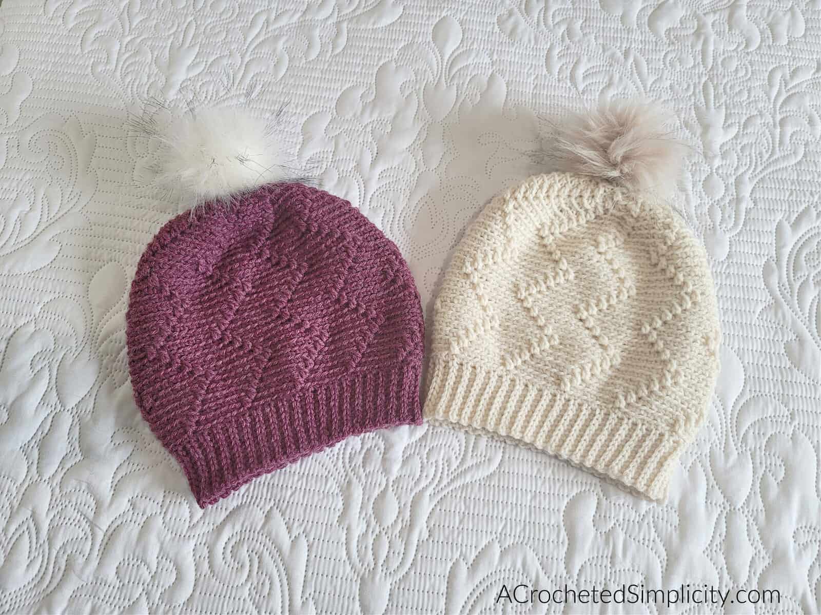 Two crocheted slouch hats laying on white bedspread.