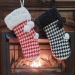 Two crochet houndstooth Christmas stockings with faux fur cuffs hanging on the front of a fireplace.