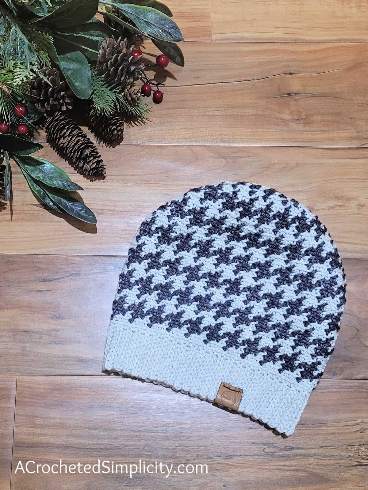 Charcoal grey and cream houndstooth crochet hat laying on a wood floor.