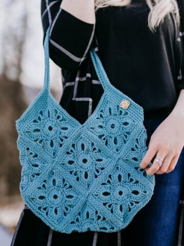 Close up of woman holding blueish green crochet market tote.