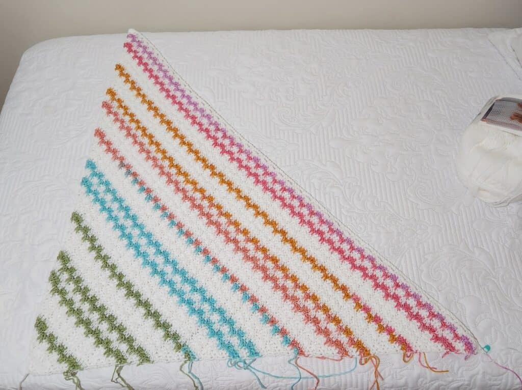 Close up of a striped colorful c2c blanket in progress spread on a white surface.