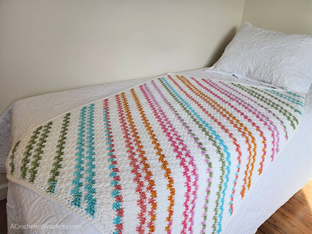 Crochet colorful striped c2c blanket laying on a twin bed.