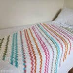 Crochet colorful striped c2c blanket laying on a twin bed.