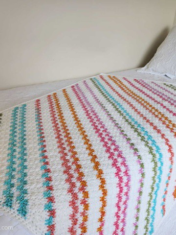 Crochet colorful striped c2c blanket laying on a twin bed.