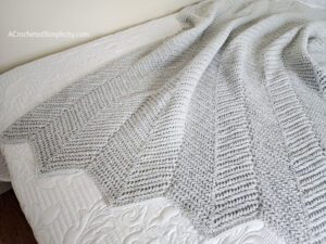 Herringbone Single Crochet Ripple Stitch Blanket in grey laying on bed.