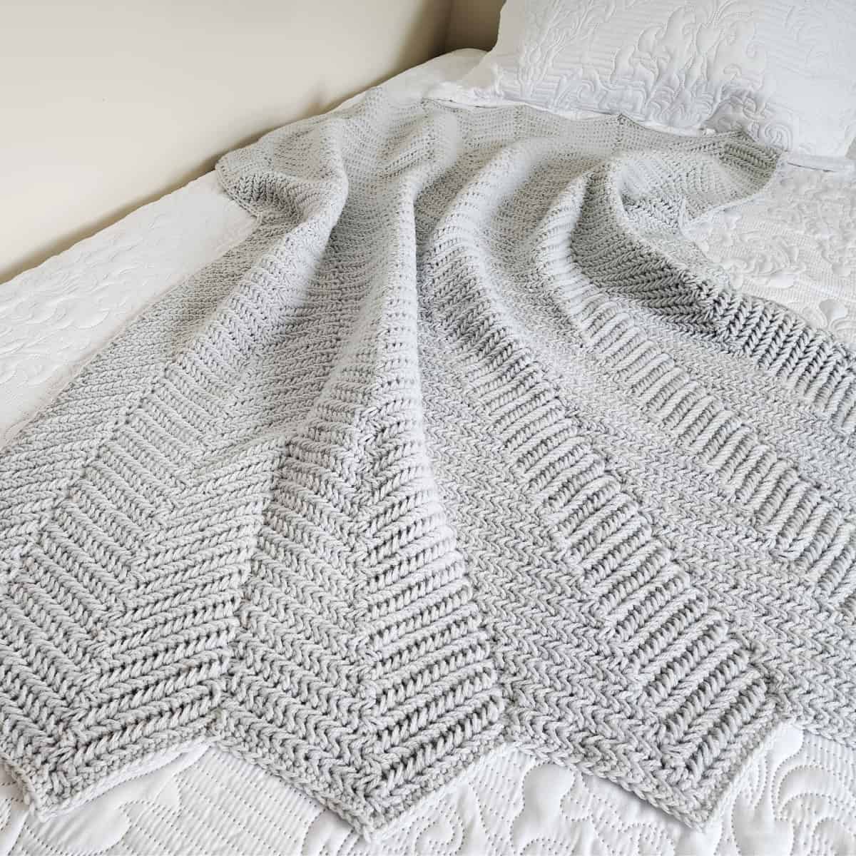 Light grey crochet ripple blanket laying on bed.