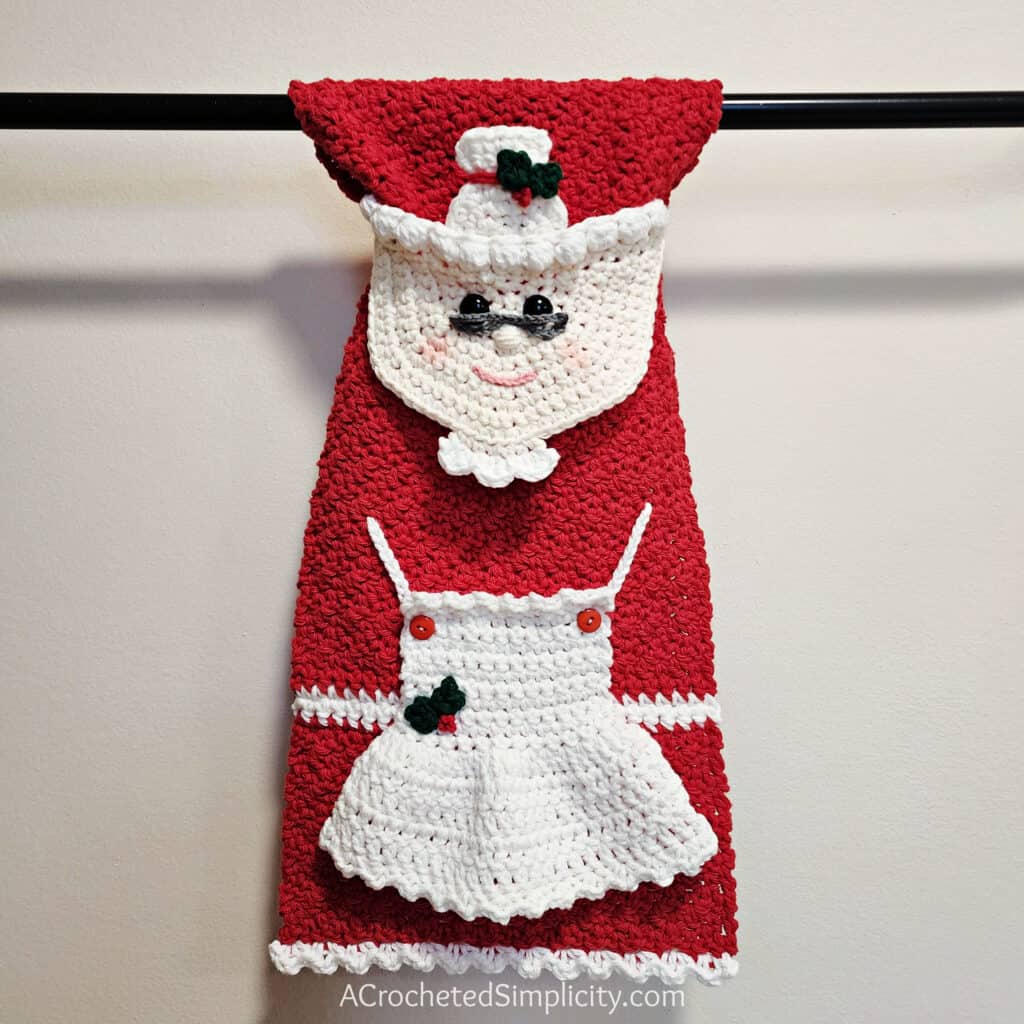 A crochet Mrs. Claus keyhole kitchen towel hanging on a towel bar.