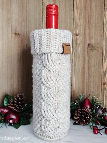 Cabled crochet wine cozy with a bottle of wine and holiday decor.