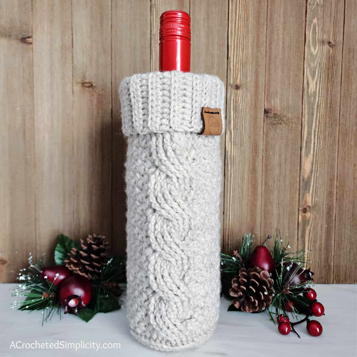 Cabled crochet wine cozy with a bottle of wine and holiday decor.