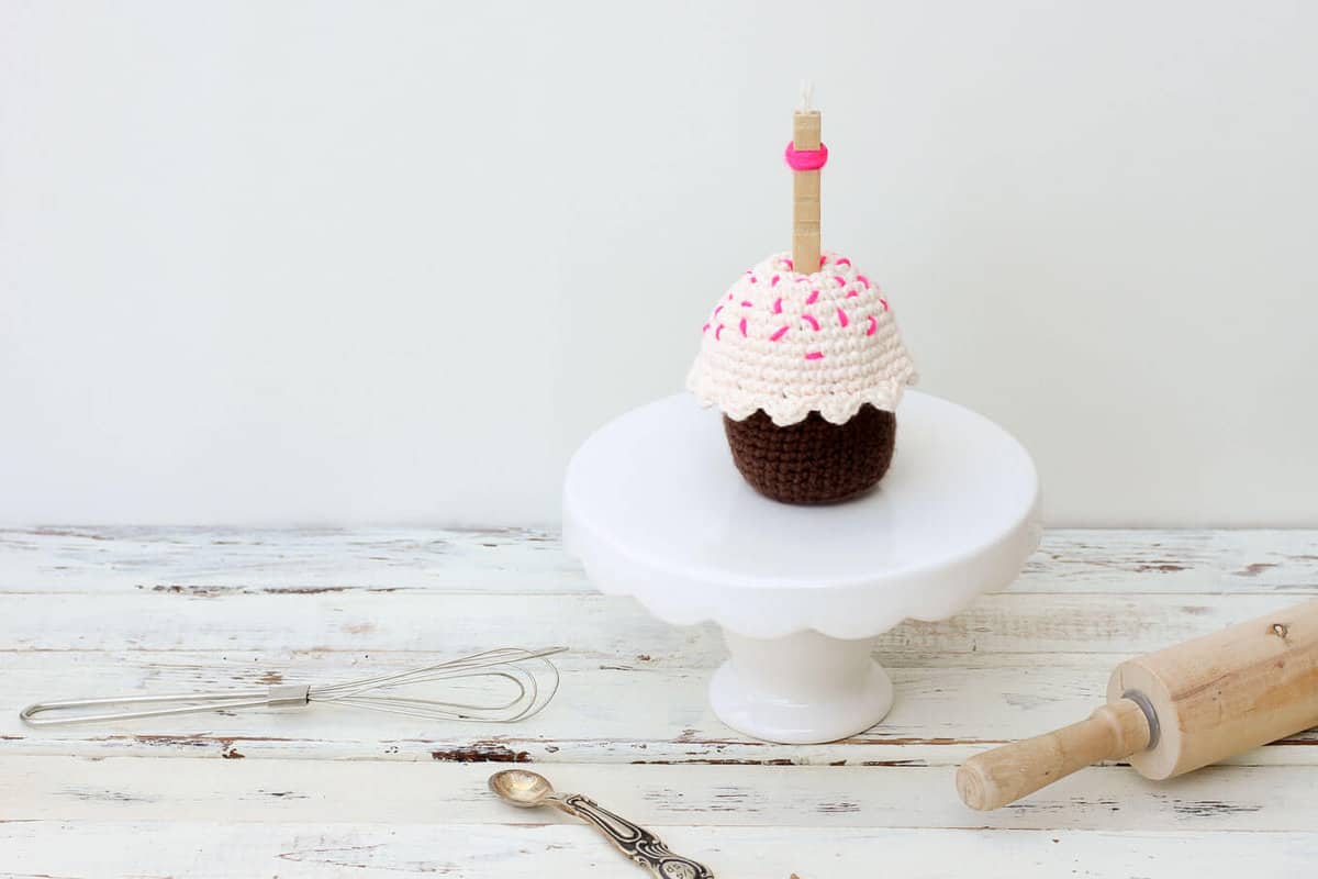 Chocolate crochet cupcake with pink frosting and sprinkles.