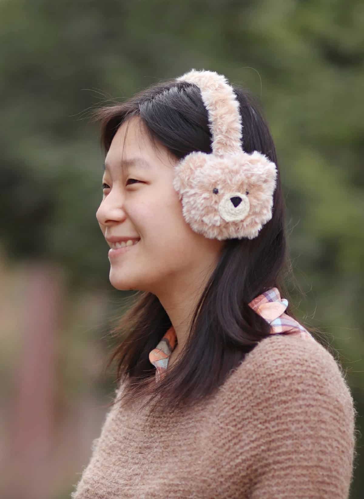 Girl smiling and modeling cute little faux fur crochet teddy bear earmuffs.