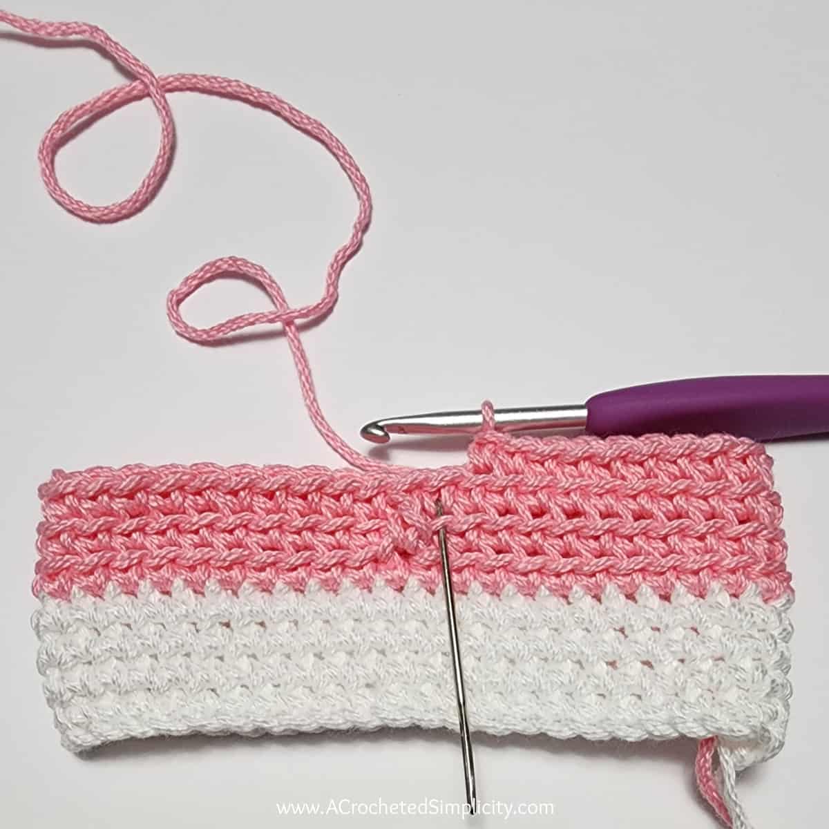 Crochet Valentine's Day treat bag tutorial photo in pink and white yarn showing where to work the next in round 2.