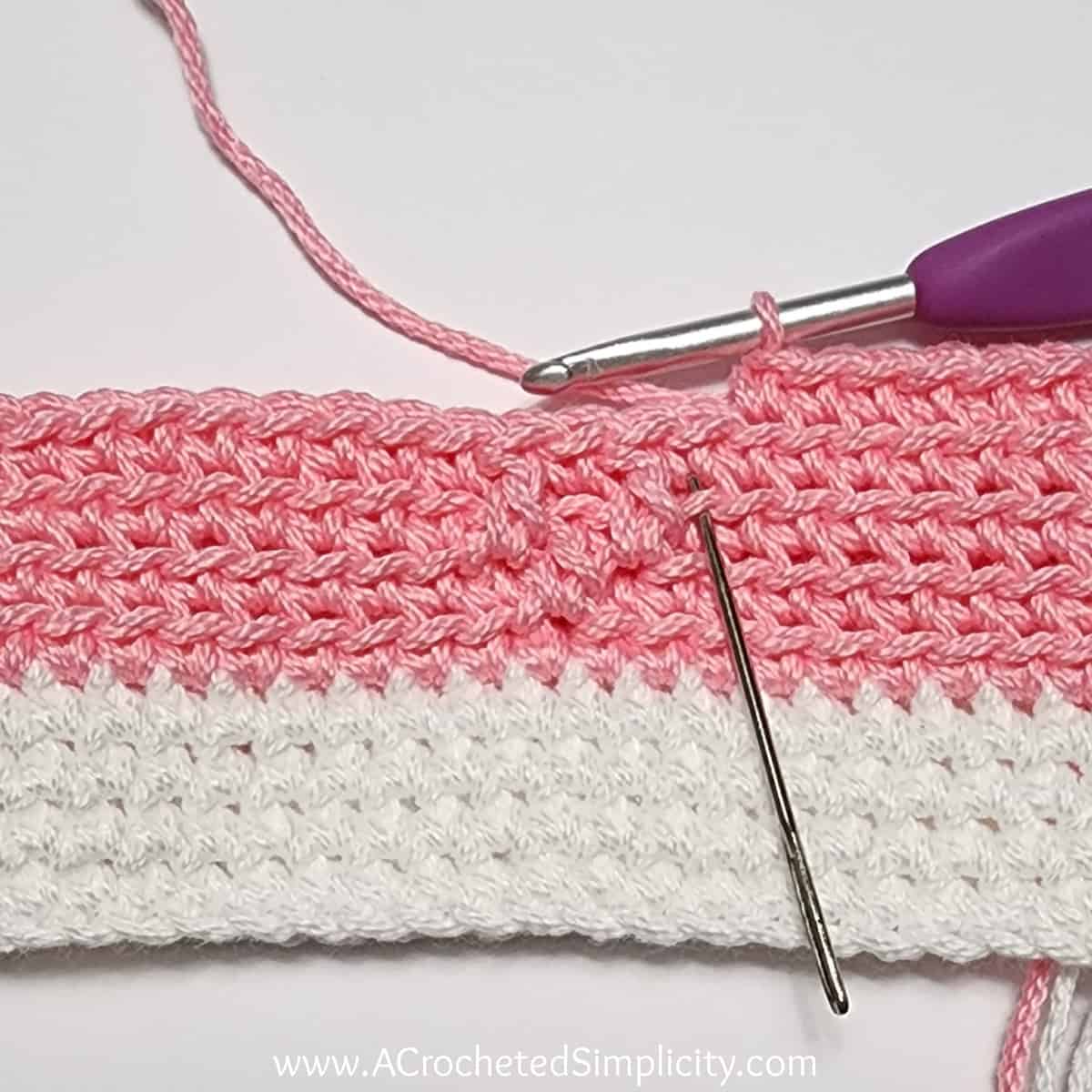 Crochet Valentine's Day treat bag tutorial photo in pink and white yarn showing where to work the next stitch in round 3.