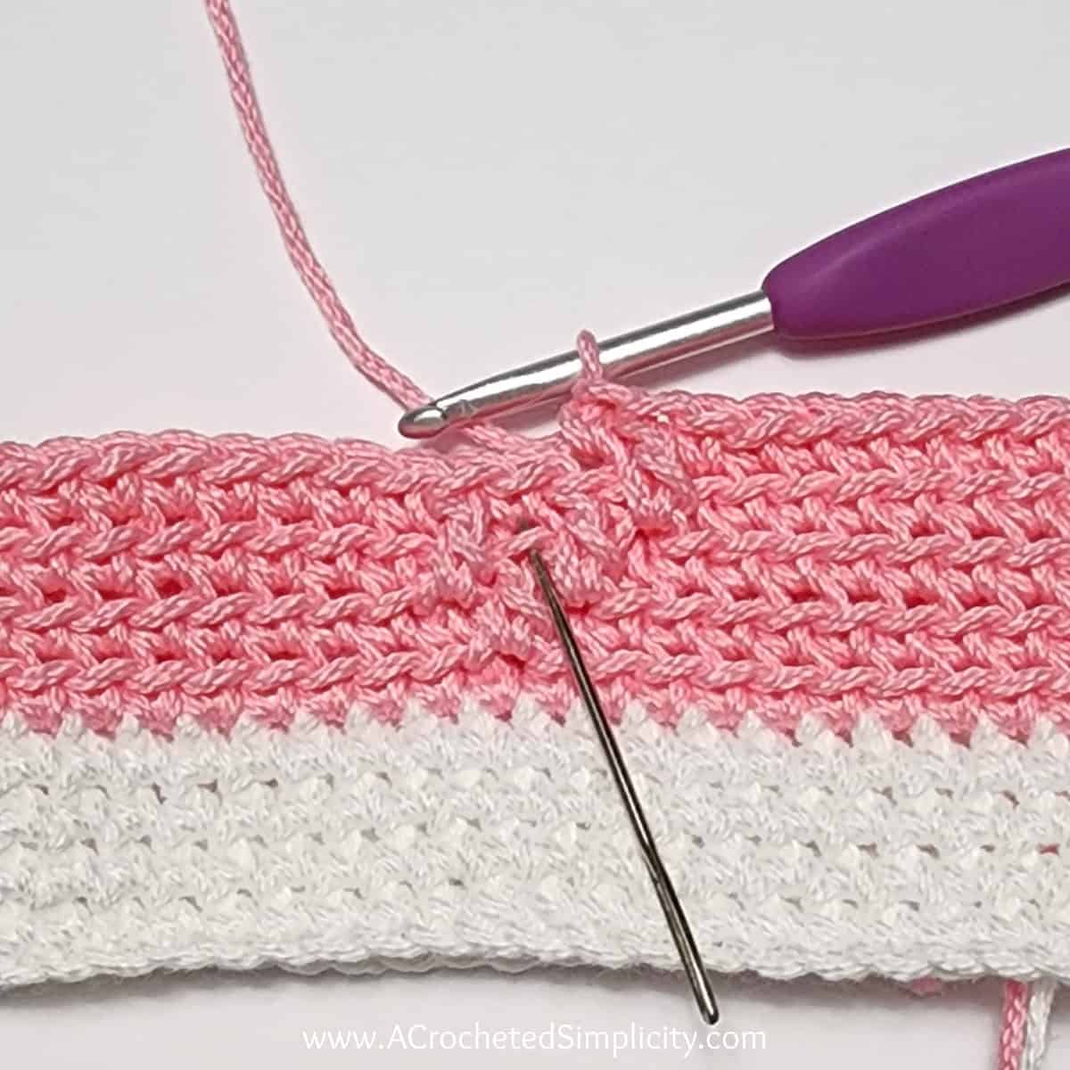 Crochet Valentine's Day treat bag tutorial photo in pink and white yarn showing where to work the next stitch in round 3.