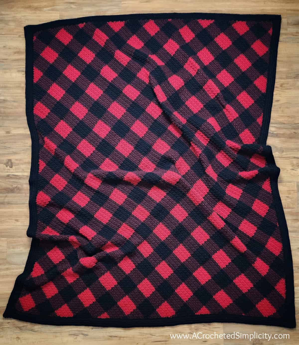 Traditional red and black c2c crochet buffalo plaid blanket laid out on wood floor.